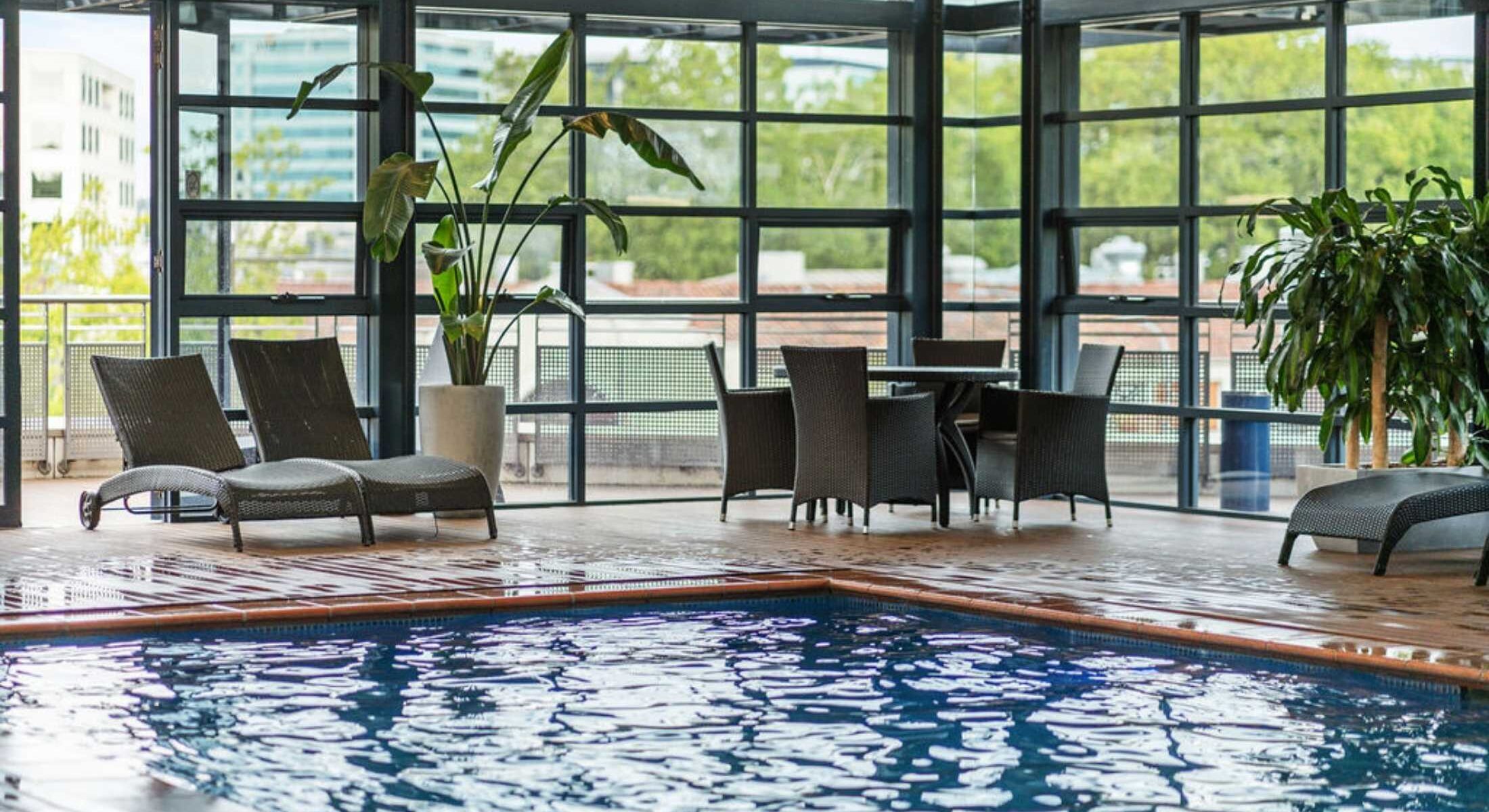 Novotel Canberra's Indoor swimming pool during daylight with the water rippling and pool side day beds